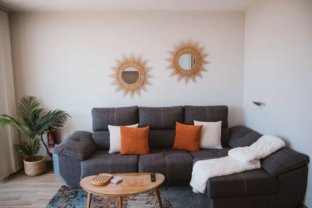 Living room of a Standard apartment with a grey sofa and sunburst mirrors