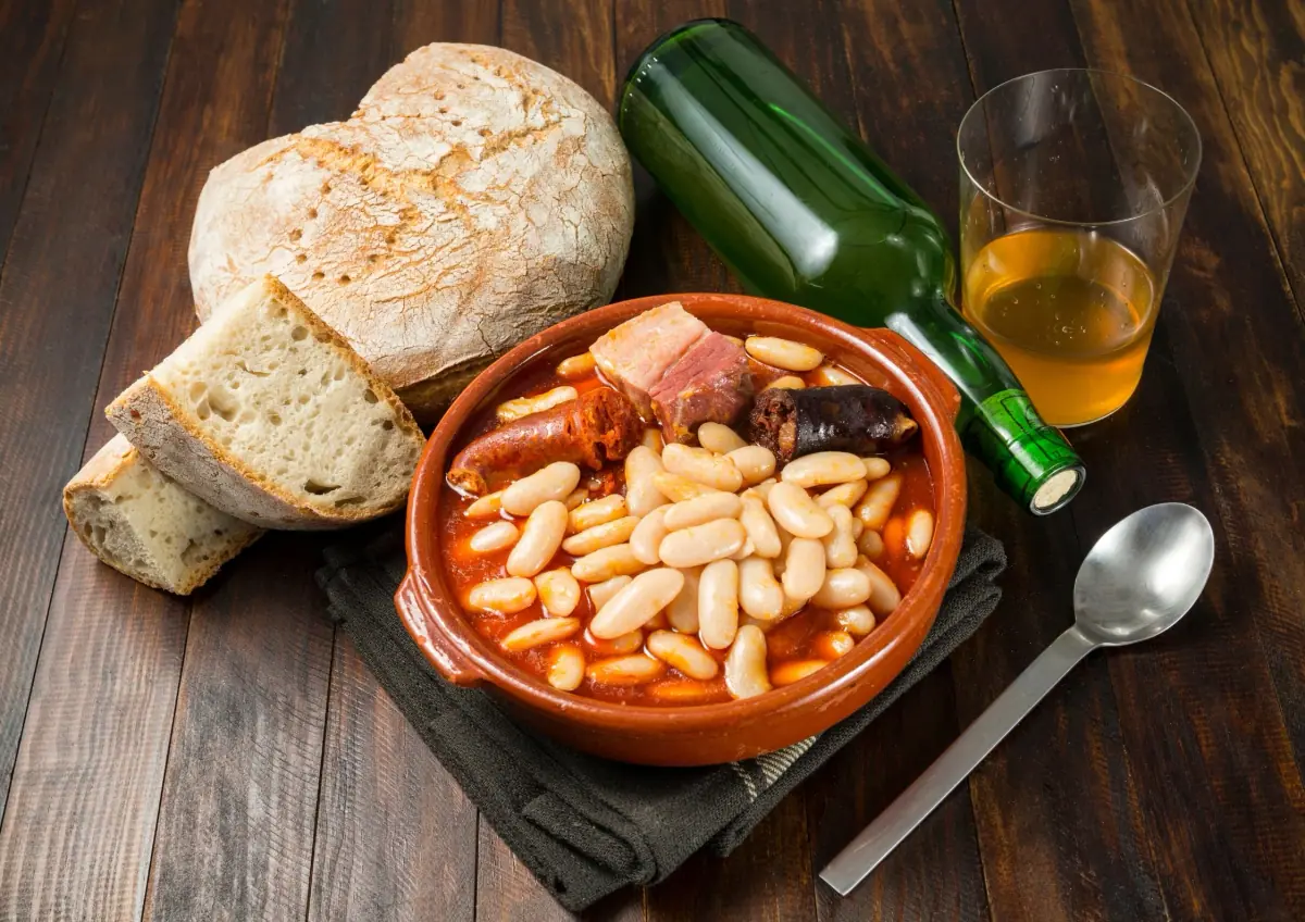 Asturian fabada in a clay pot, with bread and cider