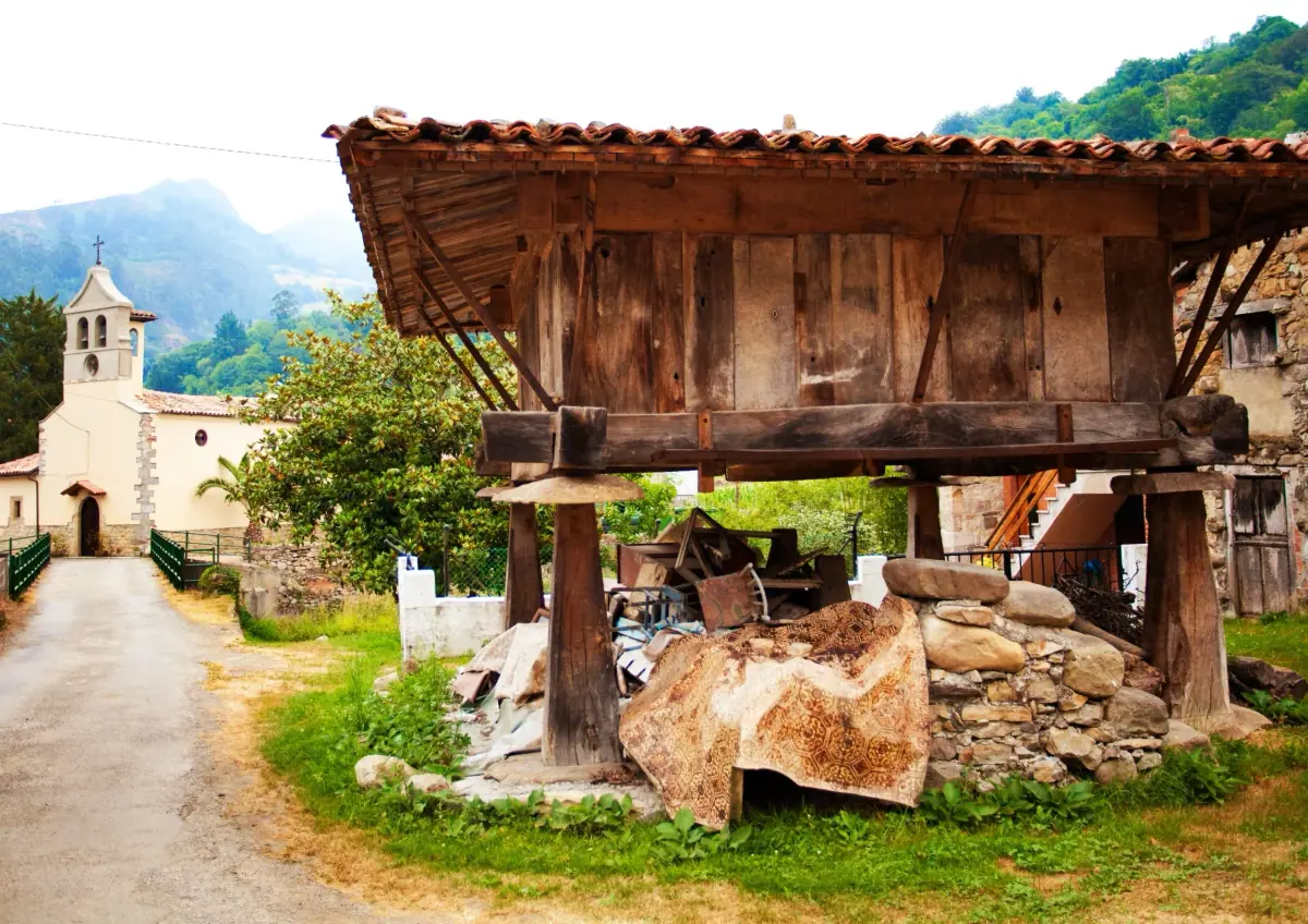 A wooden hórreo granary beside a village church