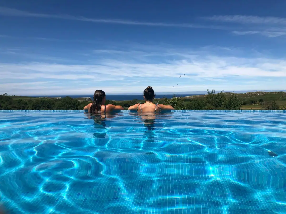 Two swimmers in the infinity pool, facing the sea