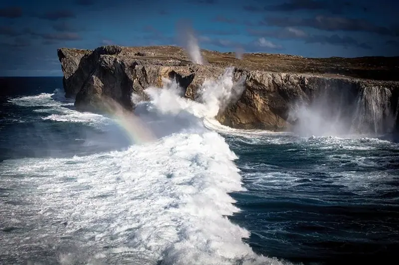 Waves breaking against the cliffs of Pría, with a rainbow