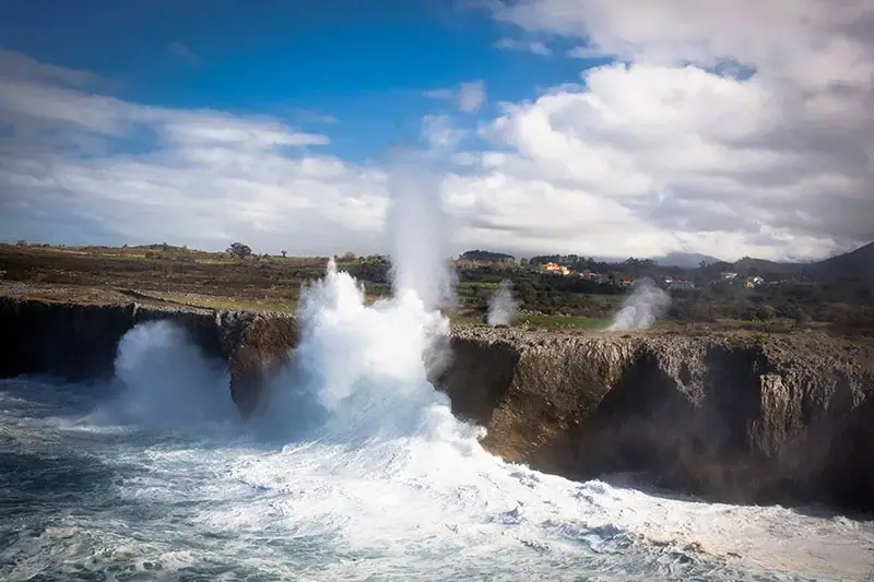 A blowhole's jet rising from the meadow above the cliff, with a heavy swell